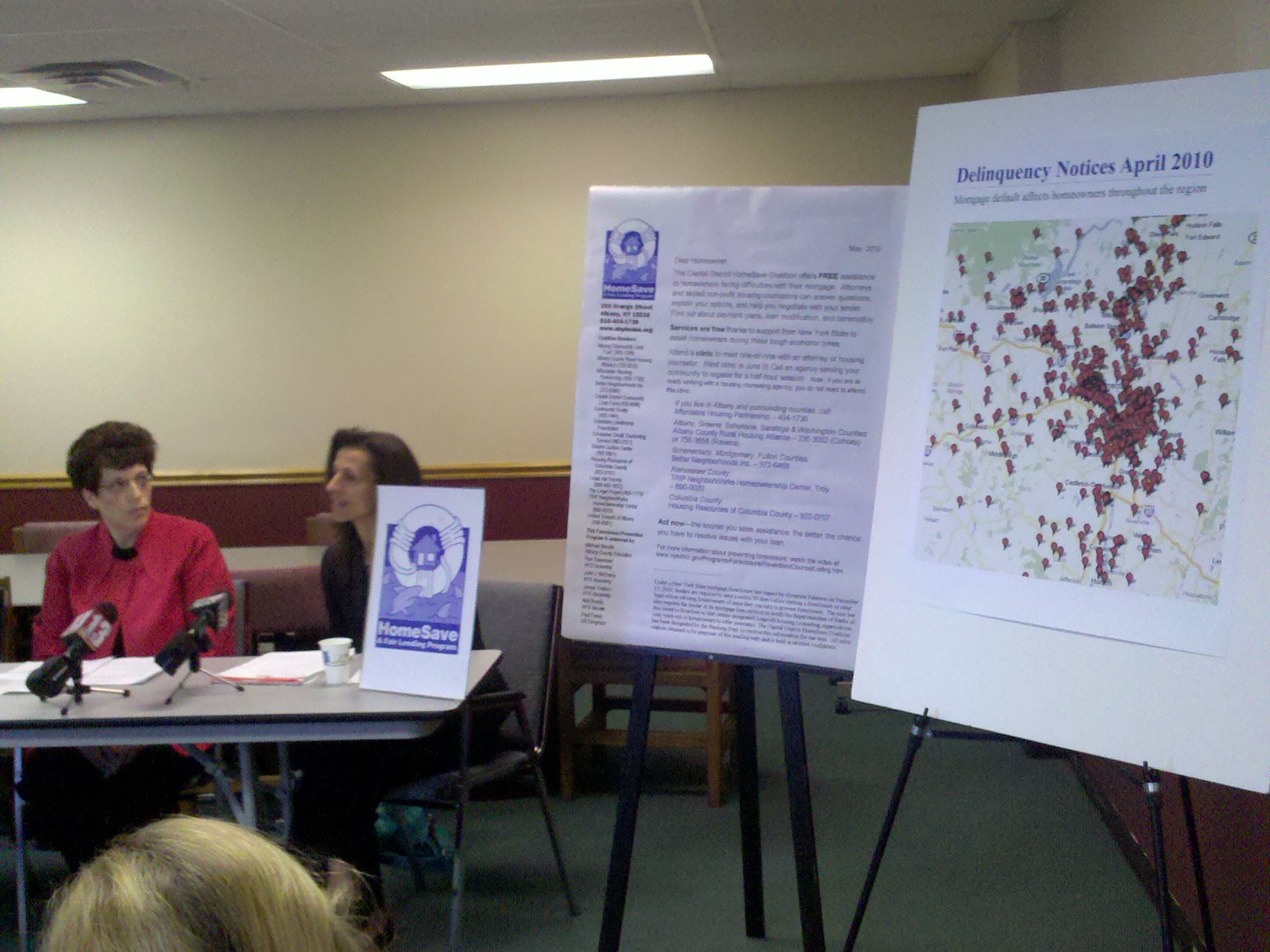 CPB Chairperson and Executive Director Mindy A. Bockstein at a table with others discussing home foreclosure rescue scams. Pictures showing the frequency and location of such scams are on display on easels. Click on this image to listen to the audio introduction to this section.